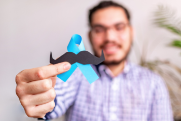 A man holding a blue ribbon with a black mustache on it to represent Movember month.
