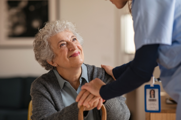 An elderly woman smiling at a medical professional as they hold her hand in support.