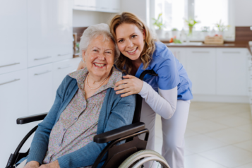 A carer hugging an elderly woman who is sitting on a wheelchair.