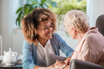 A young woman smiling and holding the hands of an elderly woman to comfort her.