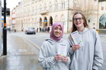 Two young healthwatch volunteers standing together outside and holding leaflets.