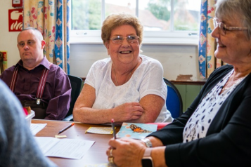 Two elderly ladies and a man sitting at a table and smiling.