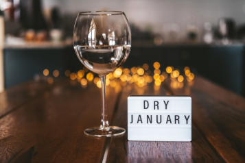 A wooden table with a cup of wine and a sign that says "dry January"