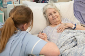 A woman lying in bed at the hospital holding a female nurse's hands.