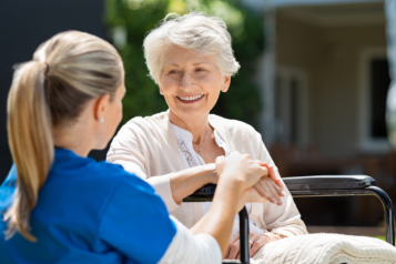 A nurse holding the hand of an elderly woman sitting on a wheelchair.