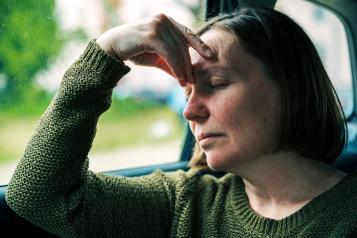 A woman sitting in the car, resting her head on her hand as she is distressed