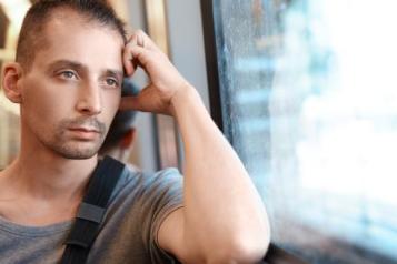 A man looking outside the window with hand on his head
