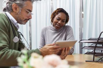 A male doctor holding a tablet device and talking to a female patient