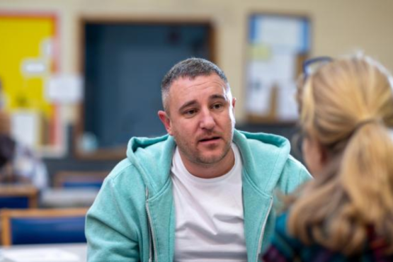Man in white shirt and blue hoodie talking to a lady.