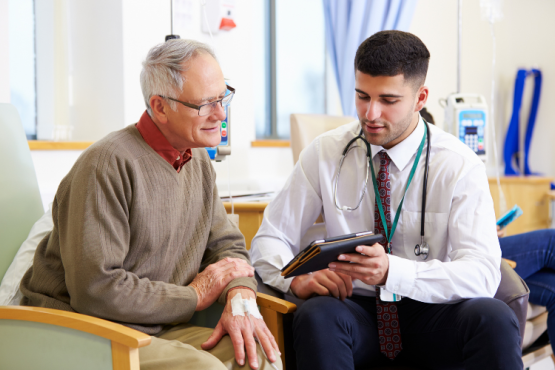 A male GP doctor holding a tablet and discussing a medical report with a male patient.
