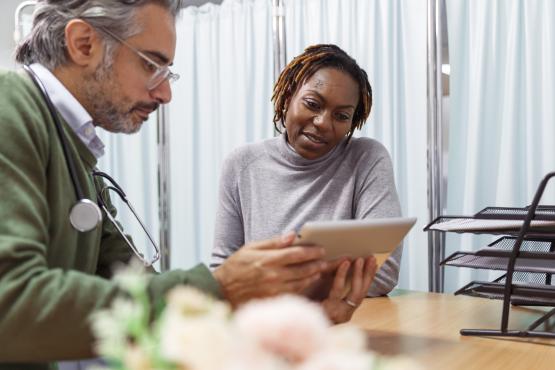 A male doctor holding a tablet device and talking to a female patient