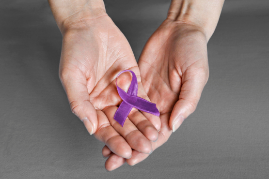 Two hands holding a purple ribbon to represent pancreatic cancer