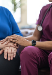 A hospice nurse in a purple uniform comforting an elderly person.